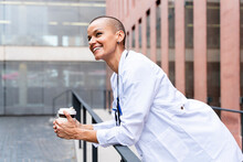 Smiling Doctor With Disposable Coffee Cup Leaning On Railing