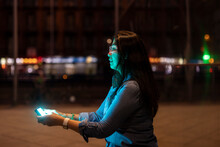 Mature Woman Wearing Smart Glasses Using Smart Phone On Footpath At Night