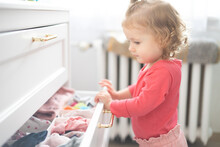 Toddler Girl Arranges Clothes And Close Drawer At Home