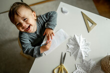 Cheerful Boy Sitting With Paper Snowflakes At Table