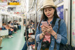 © PR Image Factory - cheerful asian woman traveler looking travel information on mobile phone by the door on a train car while riding Osaka underground in japan