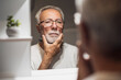 Senior man is looking at his face in bathroom and thinking about shaving beard.