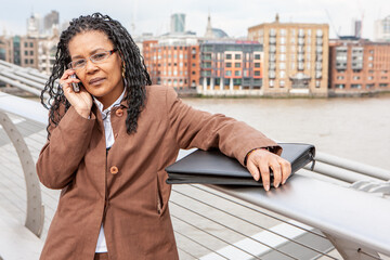 business call. a mature black business woman takes a call on her mobile phone by the river thames, l