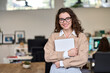 Young smiling professional business woman, happy businesswoman, female company worker intern or corporate manager holding laptop standing in modern office working, looking at camera. Portrait
