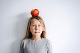 Fototapeta Mapy - Blinking with one eye boy with an apple on his head. Over white wall.