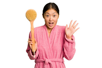 Wall Mural - Young asian woman holding a shower brush isolated receiving a pleasant surprise, excited and raising hands.