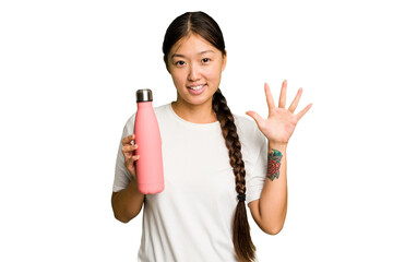 Wall Mural - Young asian woman holding a pink thermo isolated smiling cheerful showing number five with fingers.