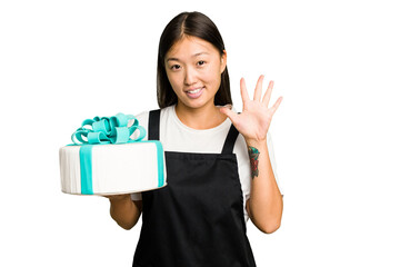 Wall Mural - Young asian bakery holding a birthday cake isolated smiling cheerful showing number five with fingers.