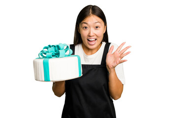 Young asian bakery holding a birthday cake isolated receiving a pleasant surprise, excited and raising hands.