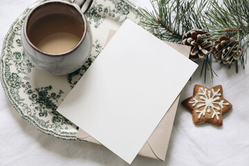 Wall Mural - Christmas still life. Blank greeting card, invitation mockup.Gingerbread cookie, cup of coffee and pine tree branches. Floral green plate. White linen tablecloth with envelope. Winter festive flatlay.