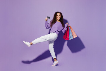 Full size side view happy young woman wear pullover hold in hand paper package bags after shopping credit bank card isolated on plain pastel light purple background. Black Friday sale buy day concept.