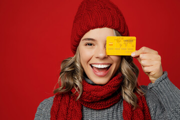 Wall Mural - Close up young fun woman wear grey sweater scarf hat hold mock up of credit bank card isolated on plain red background studio portrait Healthy lifestyle ill sick disease treatment cold season concept