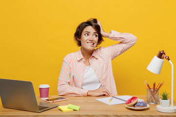 Young worried employee business woman in casual shirt sit work at office desk with pc laptop scratch hold head look aside on area isolated on plain yellow color background Achievement career concept