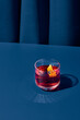 Popular cocktail negroni with gin and vermouth on blue background with shadow. Negroni cocktail on coloured background in trendy style. Contemporary concept with alcohol beverage. Bartender cocktail.