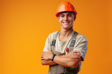 Wall Mural - Young construction worker in helmet and uniform posing on yellow background in studio