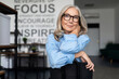 confident businesswoman with eyeglasses sitting with her arms folded comfortably on the back of a chair and looking at the camera, caucasian Middle aged older businesswoman at work Concept