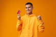 © fotofabrika - Handsome young man holding credit card on yellow color background