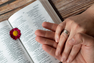 Canvas Print - Christian couple hands with rings holding in prayer over open Holy Bible Book placedon wooden background. Top view. Christian marriage relationship, love, commitment, faithfulness, biblical concept.