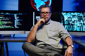 Leinwandbilder - Serious mature male software developer in smart casualwear and eyeglasses sitting against computer monitors in server room
