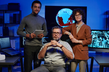 Poster - Group of three successful interculltural programmers looking at camera while two young colleagues surrounding mature IT engineer