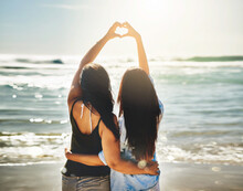 We Share A Love For Beautiful Things. Rearview Shot Of Two Friends Forming A Heart Shape Together On The Beach.