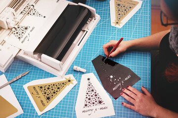 Leinwandbilder - woman with painted nails works on a christmas graphic cut from black adhesive vinyl foil. weeding procedure. holiday gift and advertisement concept. blurry background with plotter and tools