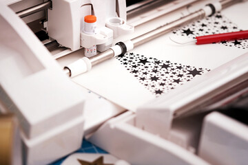 Leinwandbilder - plotting machine makes large christmas stickers arranged from star symbols out of black adhesive vinyl film. DIY holiday gift and advertisement concept. selective focus