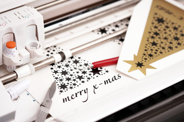 Leinwandbilder - plotting machine makes large christmas stickers with star symbols and lettering from black adhesive vinyl film. DIY holiday gift and advertisement concept. selective focus. top view