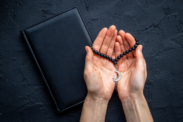 Praying hands hold black Muslim rosary with silver crescent moon