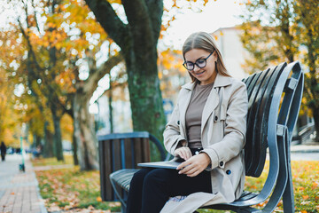 A business woman works with a laptop in Autumn Park. She has a great smile, long hair and big blue eyes. Portrait of a modern working woman. Yellow park background