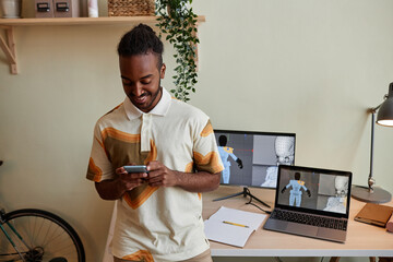 Waist up portrait of creative black man as digital 3D designer using smartphone by workplace, copy space