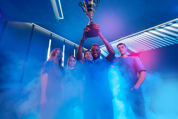 Wall Mural - Gamer team winner of video games tournament. Holding big cup trophy of victors cyber gaming esport. Soft focus, neon color