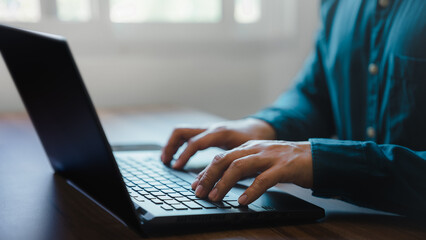 Poster - Closeup image of a young man working and typing on laptop computer keyboard on wooden table in cafe.