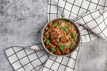 Wall Mural - Spicy beef noodle soup or ramen with herbs in bowl on a dark gray background. Top view, flat lay.