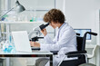 © AnnaStills - Young clinician with disability sitting on wheelchair by workplace in clinical laboratory and studying new virus in microscope