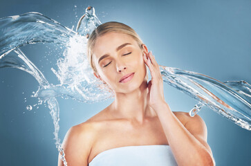 Wall Mural - Face, beauty and water splash of woman with eyes closed isolated on a blue background in studio. Skincare hygiene, facial cleaning and young female model from Canada feeling refreshed and healthy.