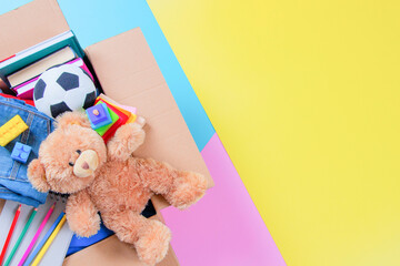 Wall Mural - Donations box with kid toys, books, clothing for charity on colorful yellow, pink, light blue background. Top view