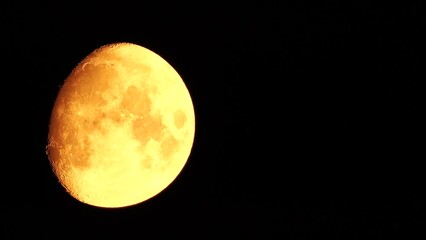 Wall Mural - A glowing golden huge moon seen from earth through the atmosphere against a starry night sky. A large moon moves across the sky, the moon moving from the left frame to the right.