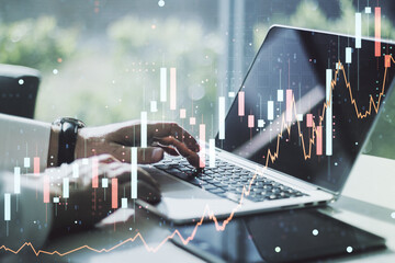 Multi exposure of abstract financial graph with hand typing on laptop on background, financial and trading concept