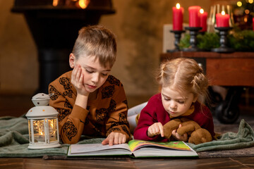 Cute preschool Children reading book fairy tales Christmas and New Year evenings at cosy candle home. Concept of family and miracle dreams.