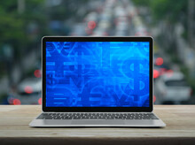 Financial Currency Symbol On Modern Laptop Computer Screen On Wooden Table Over Blur Of Rush Hour With Cars And Road In City