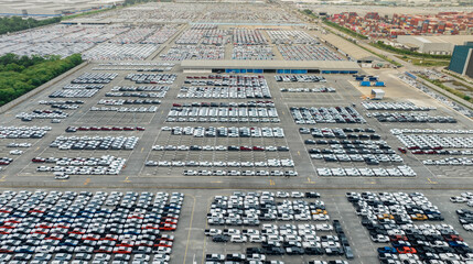 Aerial view of new cars stock at factory parking lot. Above view many cars parked in a row. Automotive industry. Logistics and supply chain business. Import or export new cars at warehouse near port.