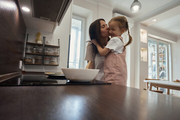 Wall Mural - young beautiful mother teaches her daughter how to cook dough in the kitchen. pancakes are baked. little helper