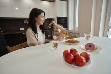 Wall Mural - family, food and people concept - happy mother and daughter have breakfast at home. Eat pancakes, have fun