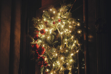 Wall Mural - Stylish christmas wreath with lights and baubles on door in evening. Modern christmas decor in city street. Atmospheric winter holidays in Europe. Merry Christmas and Happy Holidays!