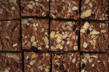 Canvas Print - Delicious homemade chocolate brownies with almond flakes and raisins cut on square slices on the baking parchment. Flat lay. Grey concrete background