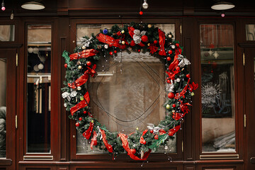 stylish christmas wreath red ribbon and baubles on building exterior. modern christmas decor in city