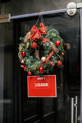 Wall Mural - Stylish christmas wreath red bow and baubles and Sorry we closed sign on doors of building. Modern christmas decor in city street. Winter holidays in Europe. Merry Christmas