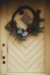 Wall Mural - Stylish christmas wreath with fir branches and red berries on doors of building. Modern christmas decor in city street. Winter holidays in Europe. Merry Christmas and Happy Holidays