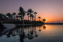 Sunset And Palm Trees With Reflection In The Pool.